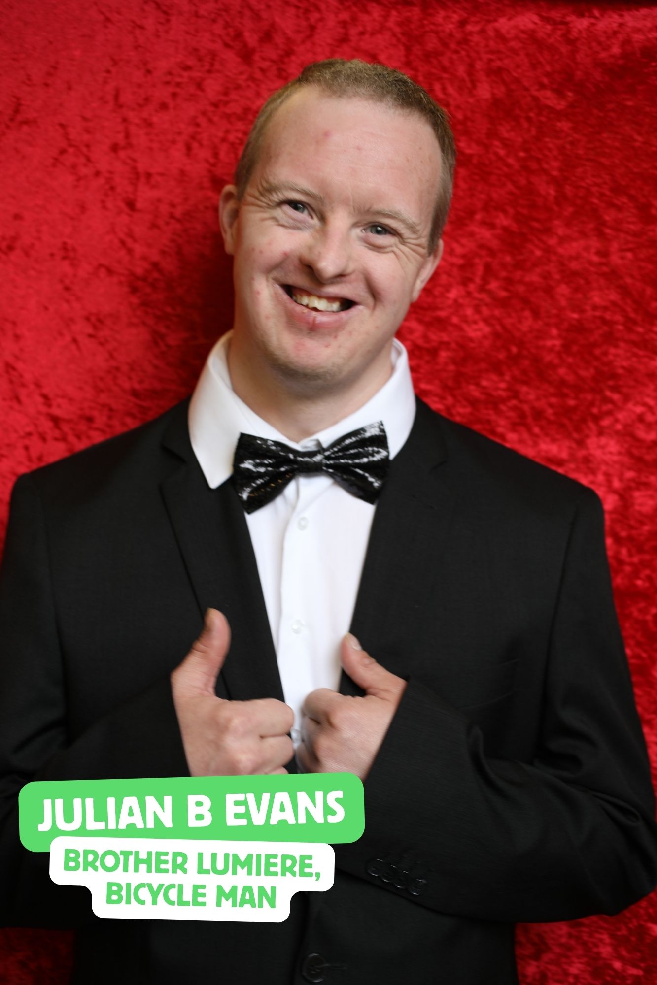 Julian, a white man in his 30's with Downs Syndrome, is playing one of the Lumiere brothers. He is wearing a black suit and bow tie and smiling at the camera.