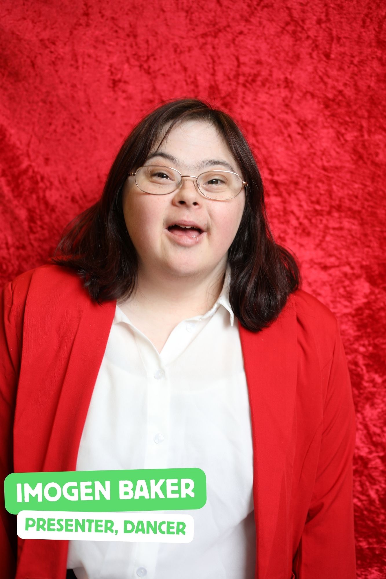Imo, a white woman with dark brown hair and Downs Syndrome, is playing the presenter. She is wearing a red blazer.