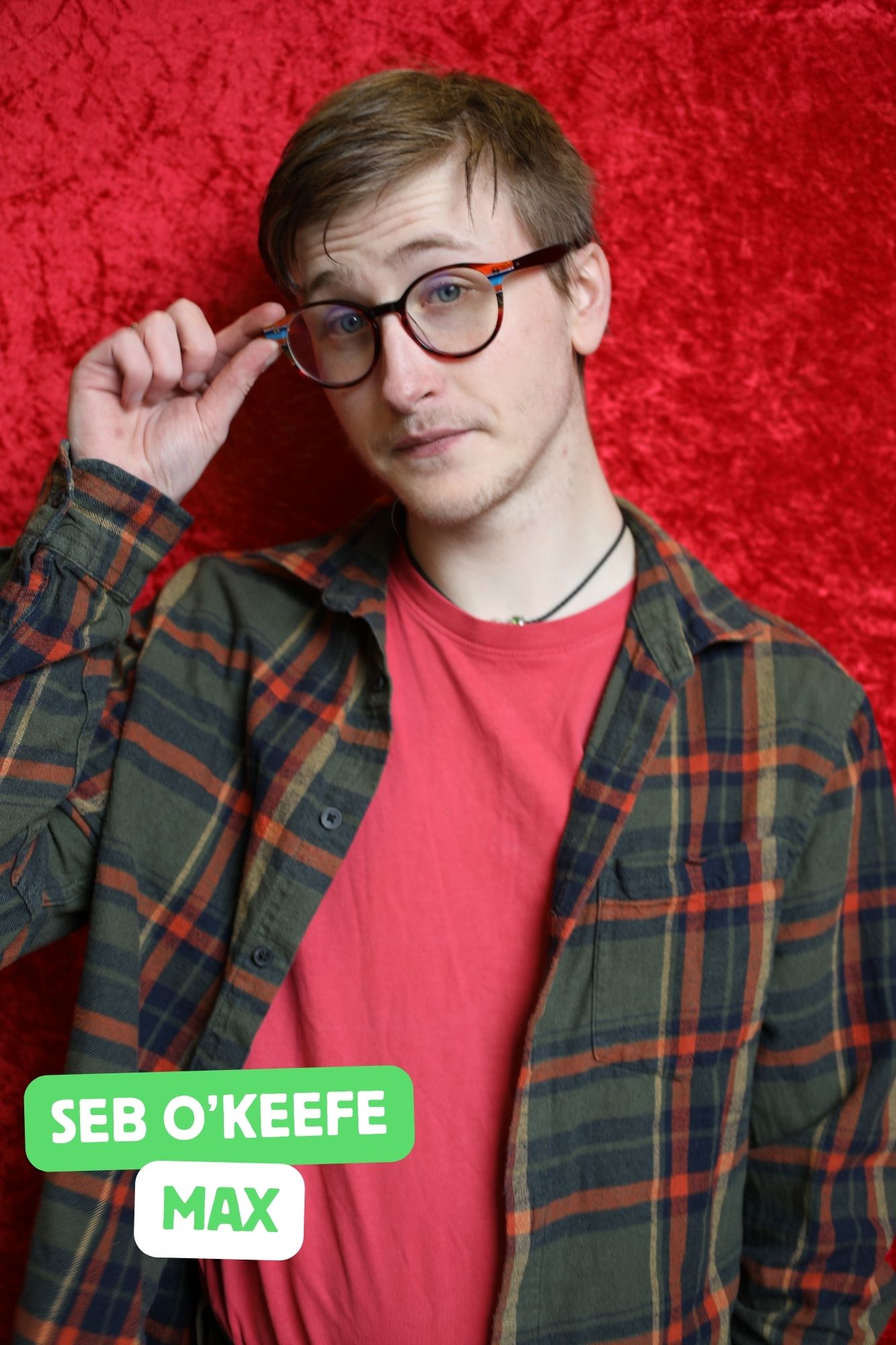 Seb, a white man with dyed hair is playing Max. He is wearing chinos and a plaid overshirt.