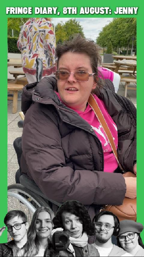 Jenny a white woman with brown hair smiles at the camera. Jenny is a wheelchair user. She is wearing a big, puple coat.