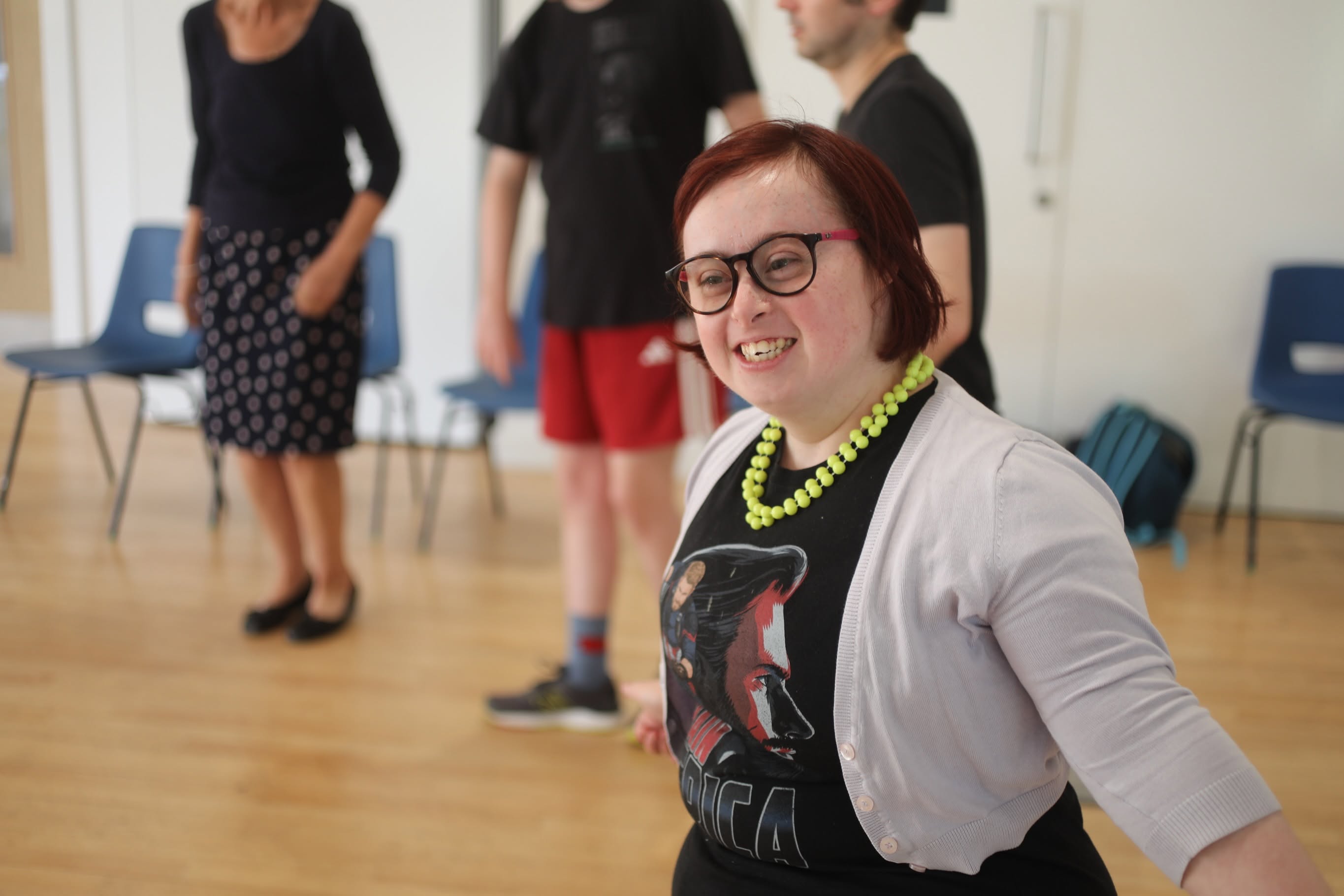 A smiling Bedazzle performer takes part in a theatre session, with other group members standing in the background.