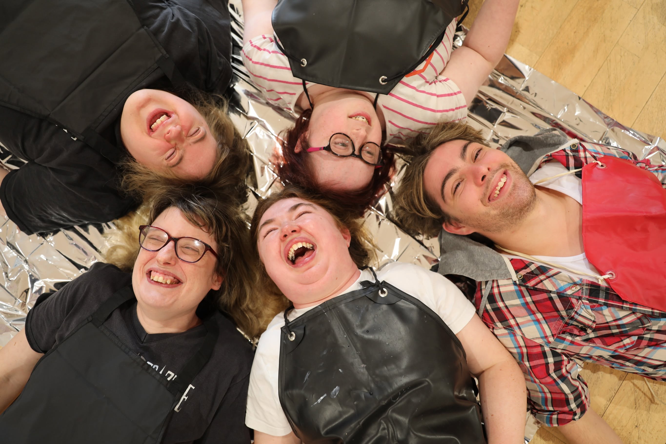 ive Bedazzle performers lie in a circle with their heads together, laughing during a creative theatre activity.